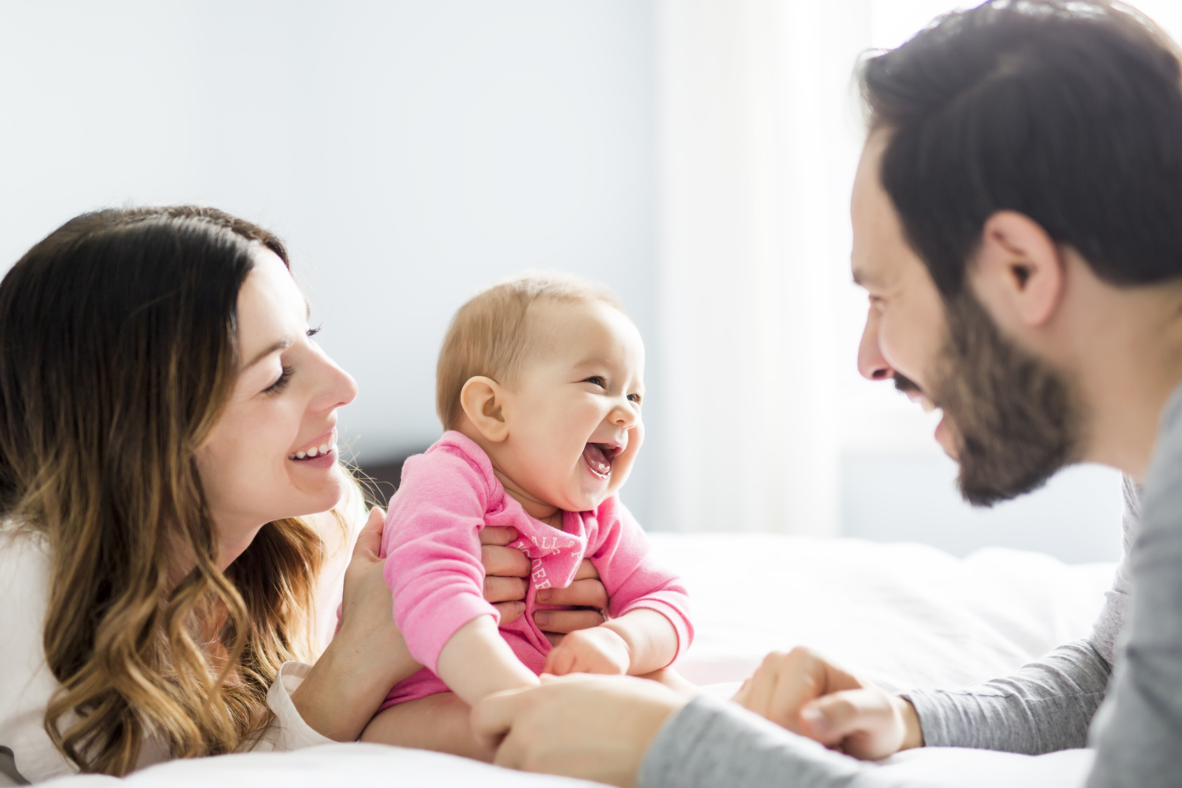 Mother father and baby child on a white bed. IVF - Learn more from ParryScope and Positive Steps Fertility