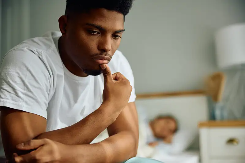 Man sitting on his bed looking concerned while learning about male infertility causes and fertility treatment options at Positive Steps Fertility