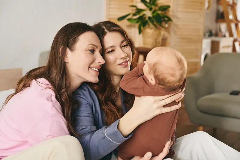 Lesbian couple smiling with their baby after growing their family through LGBTQIA+ fertility care at Positive Steps Fertility in Mississippi and Louisiana