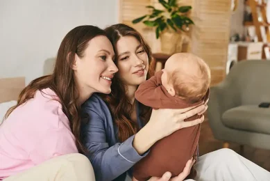 Lesbian couple smiling with their baby after growing their family through LGBTQIA+ fertility care at Positive Steps Fertility in Mississippi and Louisiana