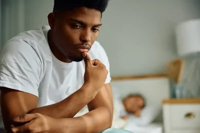 Man sitting on his bed looking concerned while learning about male infertility causes and fertility treatment options at Positive Steps Fertility